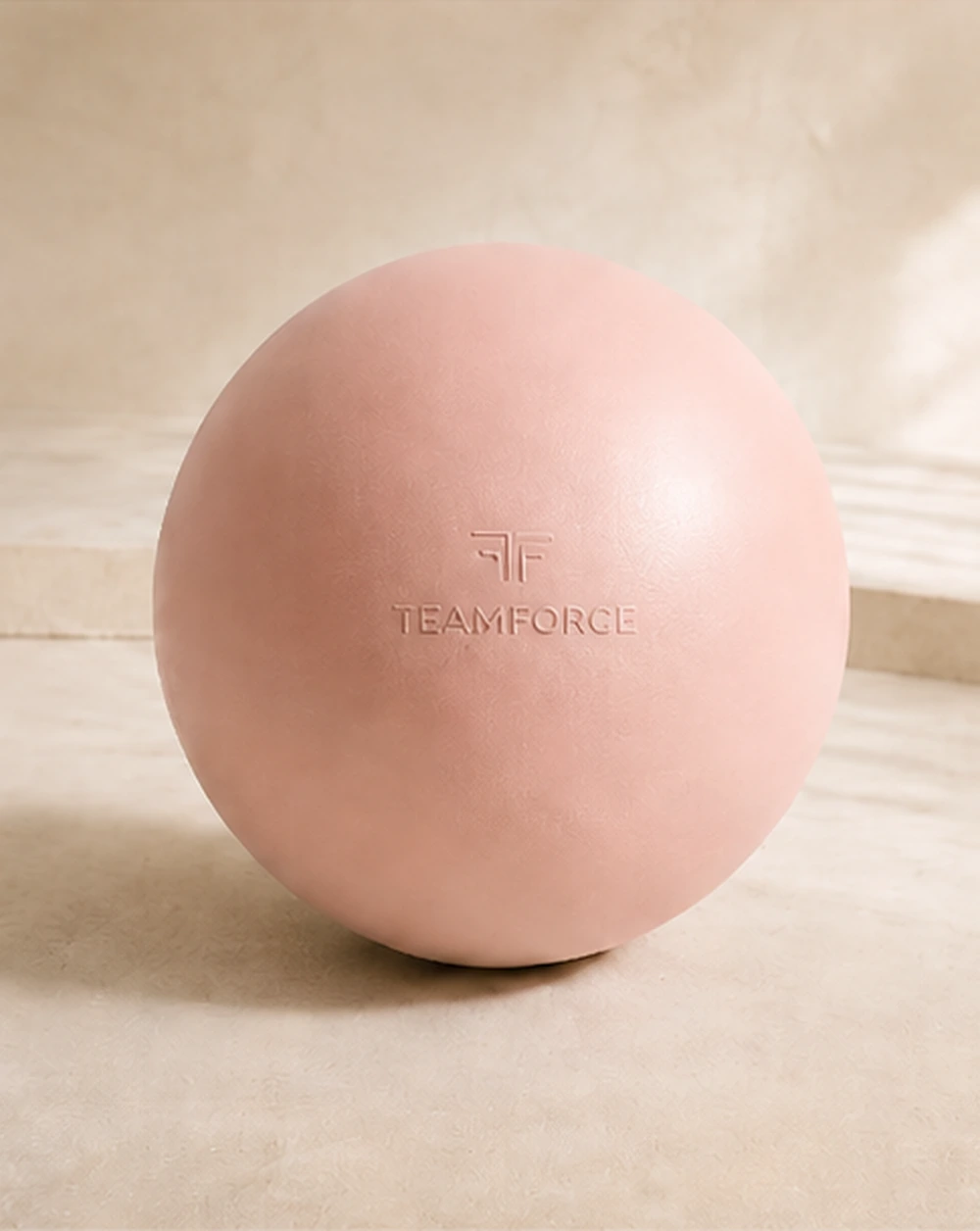 Blush Pilates ball with embossed Teamforce logo in a warm premium studio setting.