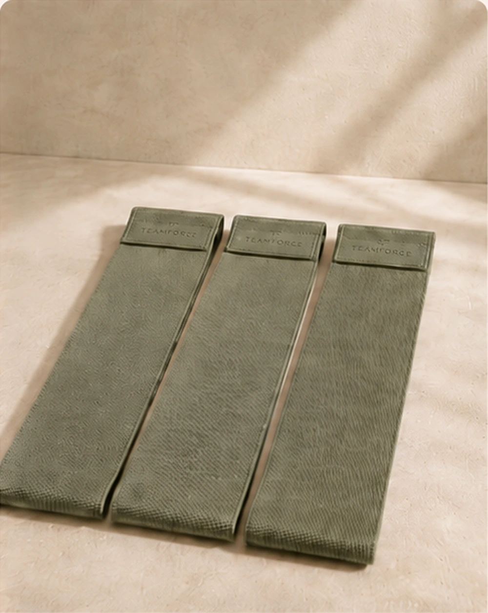 Olive green Pilates resistance bands photographed on warm stone with soft natural light.